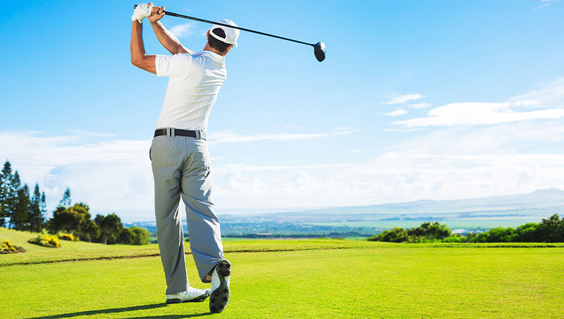 Golfer swinging club at golf ball